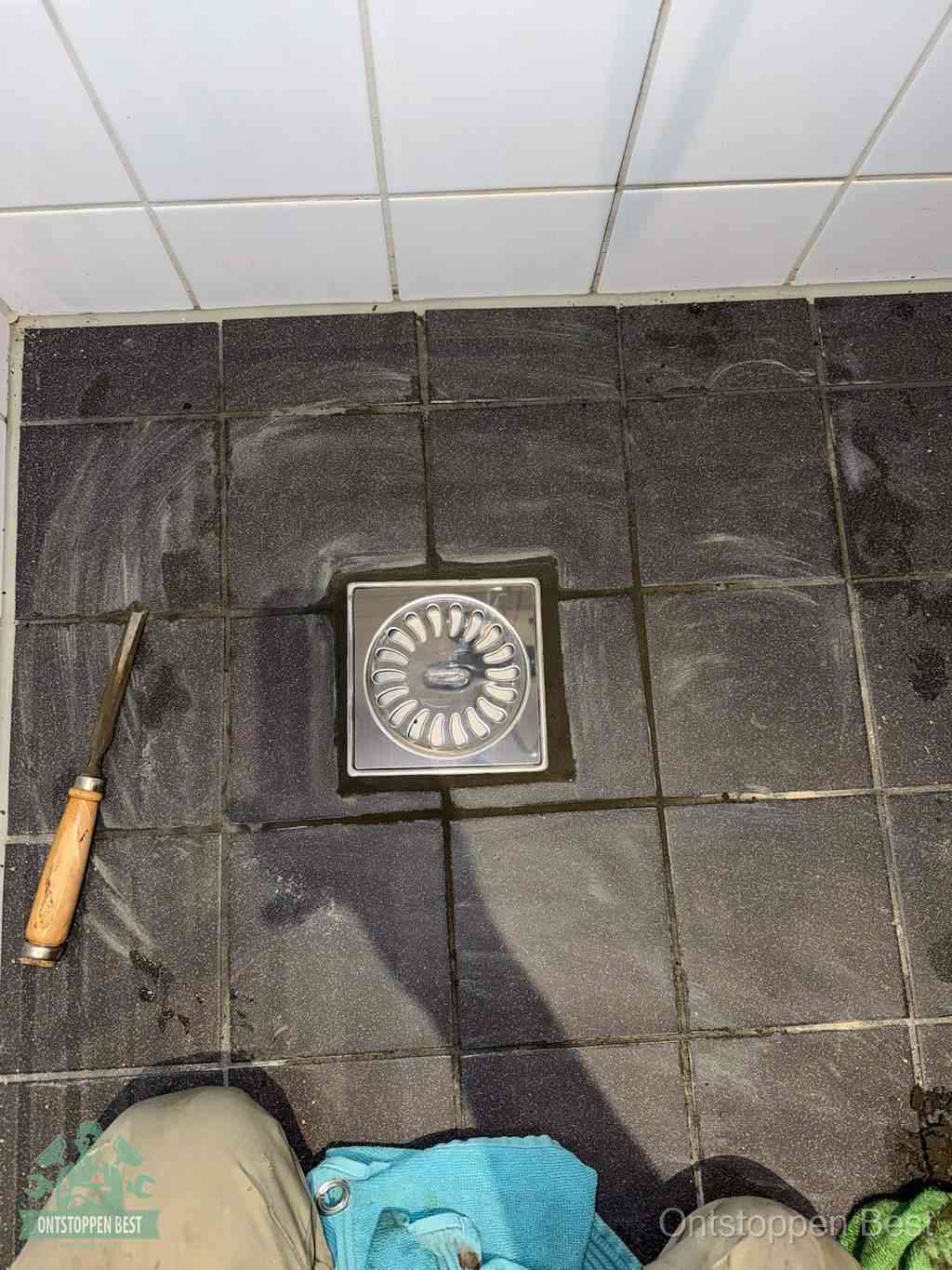 Een RVS doucheputje in een betegelde badkamervloer, zelf je badkamer ontstoppen in Best