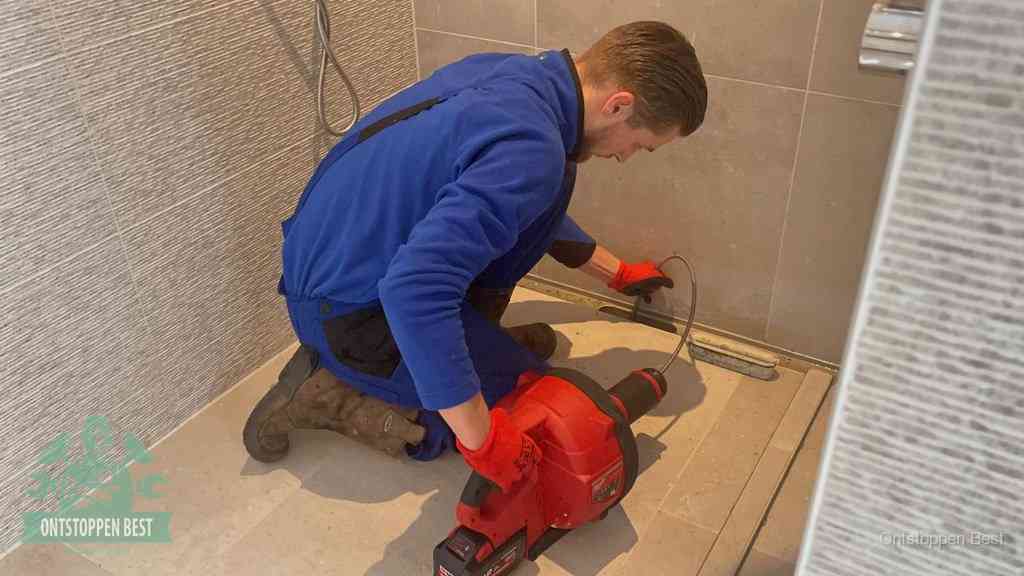 Een monteur ontstopt een langwerpige douchegoot met een elektrische veer, een doucheputje verstopt door haren en zeep in Best