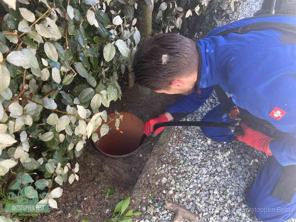 Een monteur voert een slang in een geopende rioolput in de tuin om het hoofdriool te ontstoppen in Best