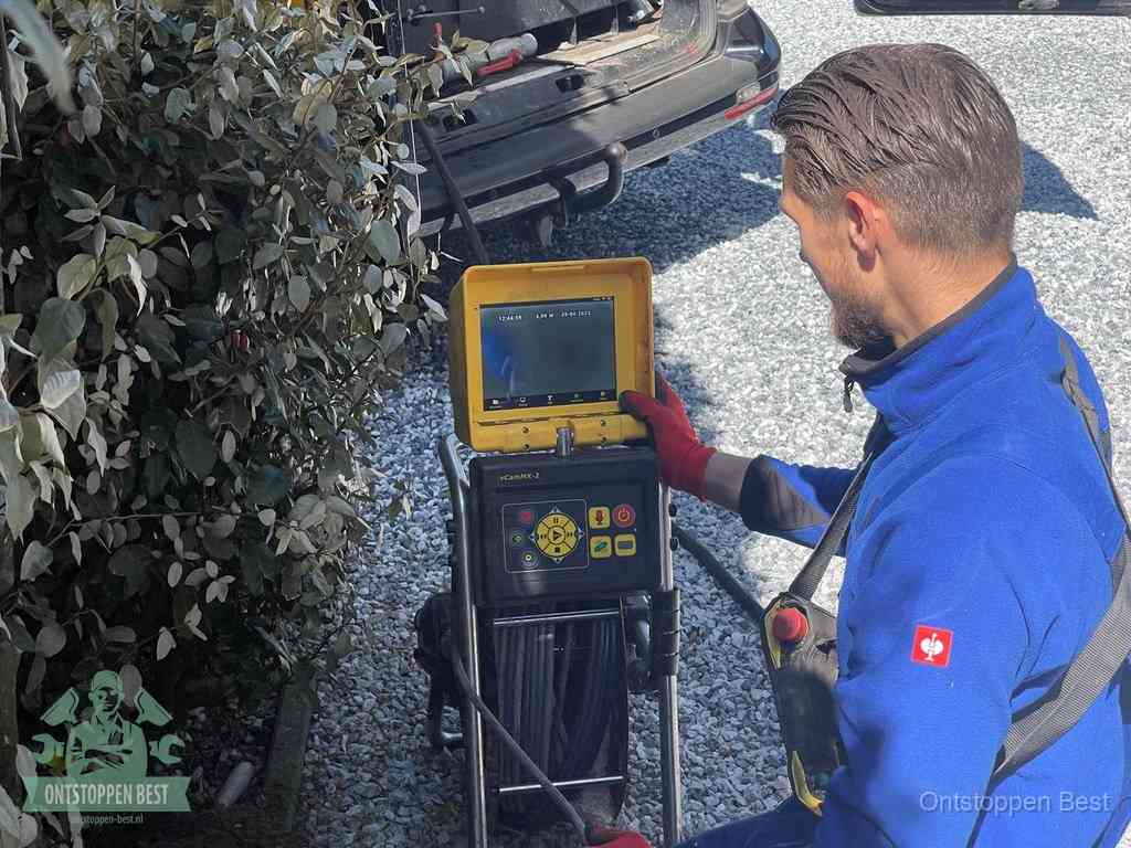 Een monteur bedient een rioolinspectiecamera met monitor en haspel om de verstopping in beeld te brengen in Best
