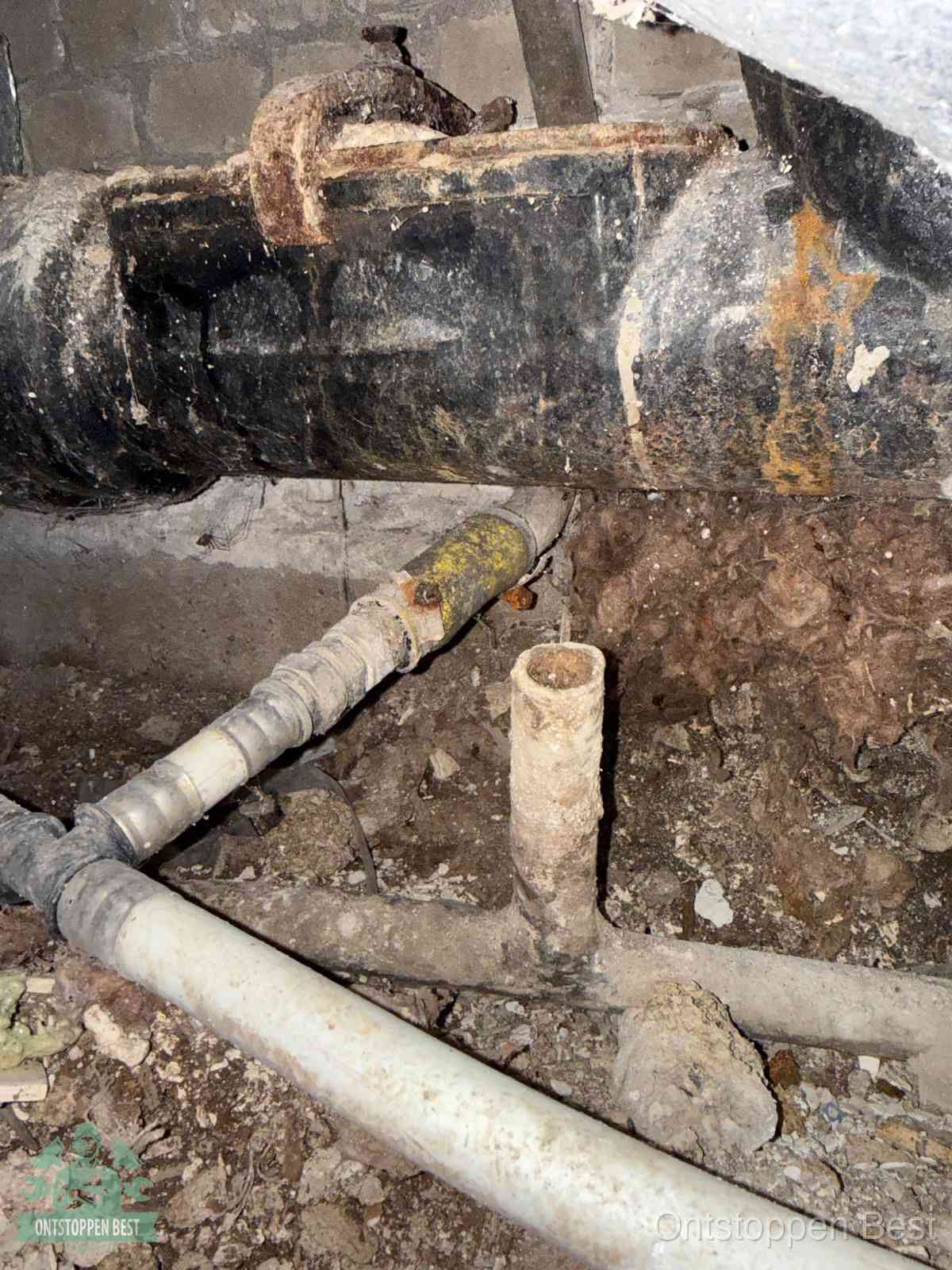 Een oude hoofdrioolbuis met roest- en kalkaanslag in een kruipruimte, oorzaak van terugkerende structurele rioolproblemen in Best